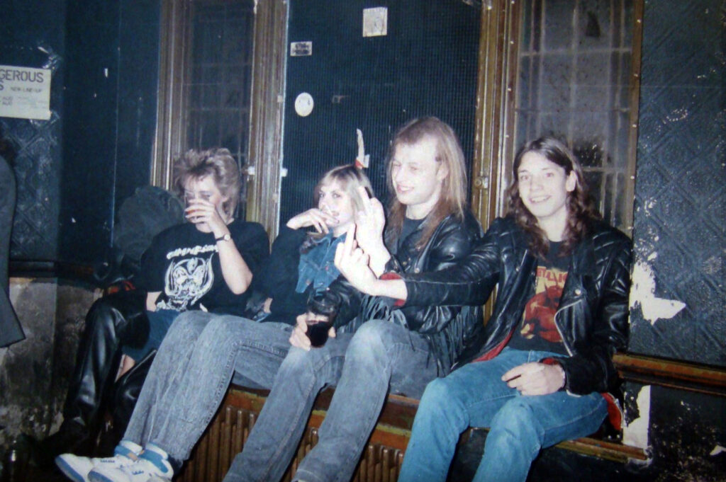 Four friends in leather jackets drinking and chatting in a dimly lit room at The Ruskin Arms.
